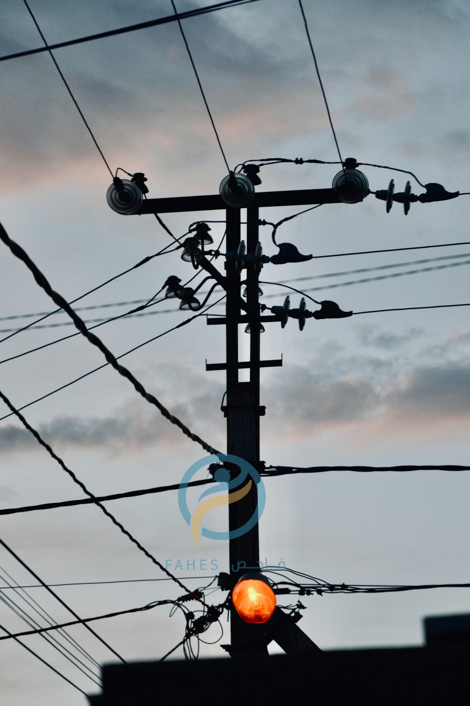 a traffic light sitting below power lines under a cloudy sky